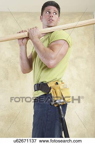 Man wearing tool belt carrying piece of wood on shoulder View Large Photo Image Stock Photo - Man wearing tool belt carrying piece of wood on shoulder. Fotosearch