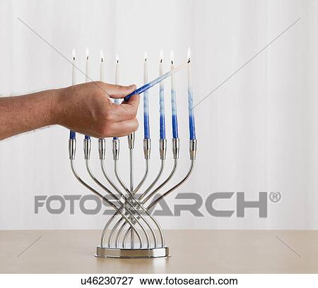 Stock Photo - Man's hand lighting menorah. Fotosearch