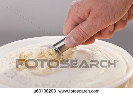 Stock Image - Mans hand scooping vanilla ice cream from tub. Fotosearch