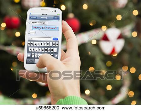 Stock Image - Man's hand sending Christmas wishes by cell phone. Fotosearch