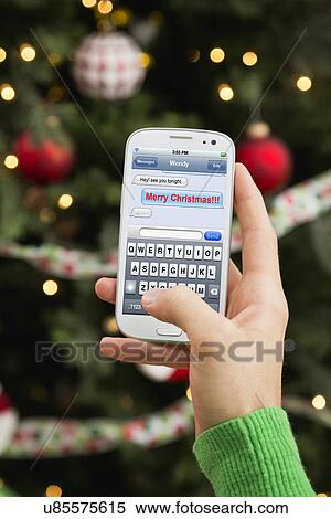 Stock Photography - Man's hand sending Christmas wishes by cell phone. Fotosearch