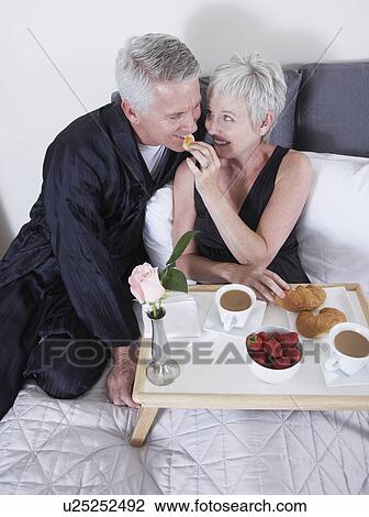 Stock Image - Mature couple eating breakfast in bed. Fotosearch