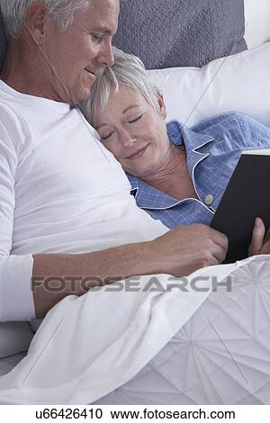Stock Image - Mature couple reading book in bed. Fotosearch
