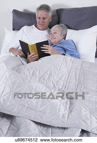 Stock Image - Mature couple reading book in bed. Fotosearch