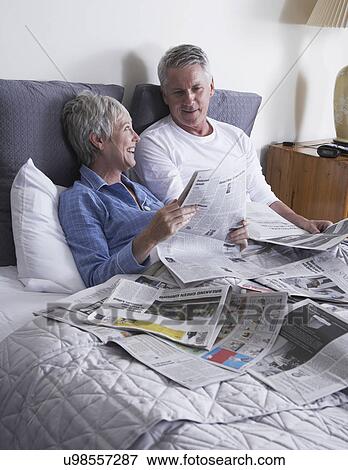 Stock Photo - Mature couple reading newspapers in bed. Fotosearch