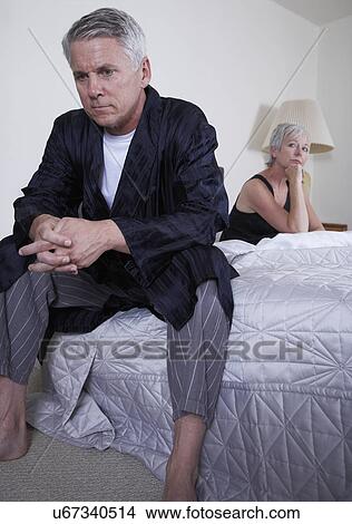 Picture - Mature couple sitting apart on bed. Fotosearch