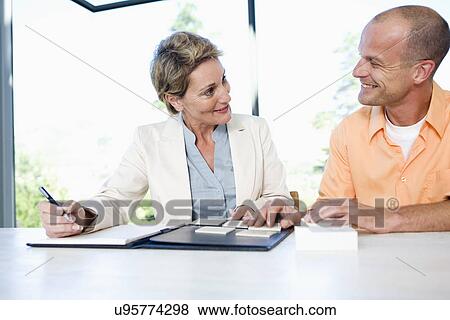 Mature man and interior designer choosing tile sample, sitting face to face, smiling View Large Photo Image Stock Photo - Mature man and interior designer choosing tile sample, sitting face to face, smiling. Fotosearch