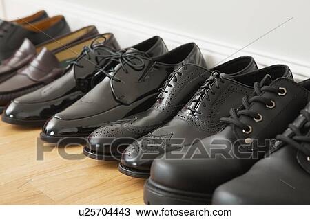 Stock Image - Men's shoes in a row against wall. Fotosearch