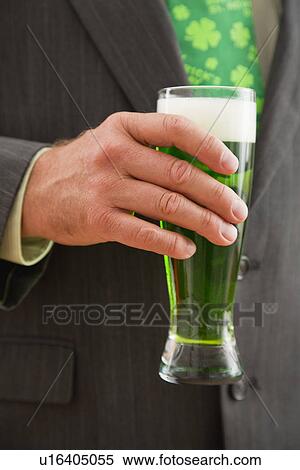Stock Photography - Mid section of man holding glass of green beer. Fotosearch