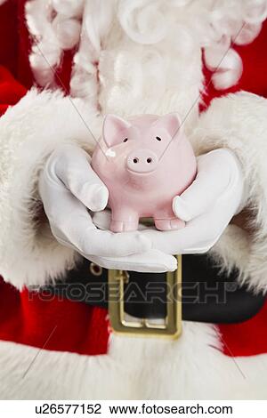 Stock Image - Mid section of Santa holding piggy bank. Fotosearch