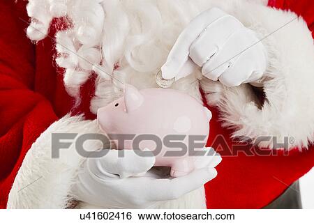 Stock Photograph - Mid section of Santa putting coin inside piggy bank. Fotosearch