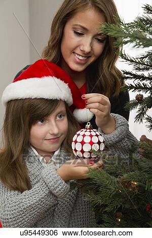 Stock Photograph - Mother and daughter (8-9) decorating Christmas tree. Fotosearch