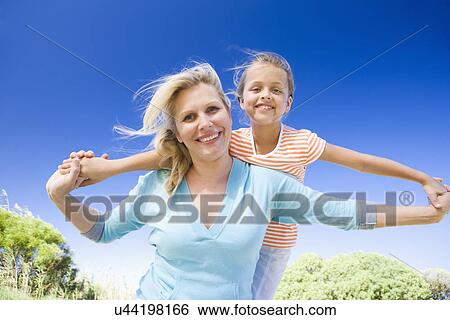 Stock Photograph - Mother carrying daughter (8-9) on shoulders. Fotosearch