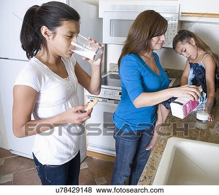 Stock Photo - Mother with two daughters (8-9, 14-15) in kitchen. Fotosearch