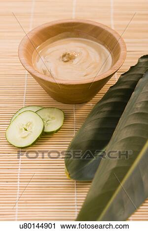 Stock Image - Mud mask, slices of cucumber and tropical plant leaves on bamboo mat. Fotosearch