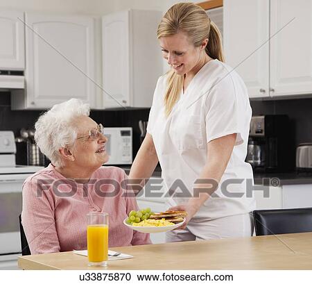 Stock Image - Nurse giving patient meal. Fotosearch