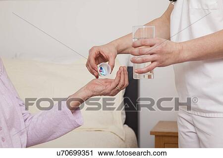Stock Image - Nurse giving pills to senior patient, close-up. Fotosearch