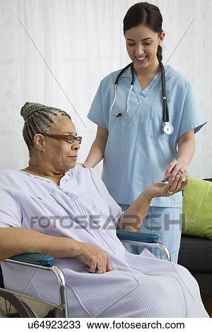 Stock Image - Nurse in nursing home giving pills to senior patient. Fotosearch