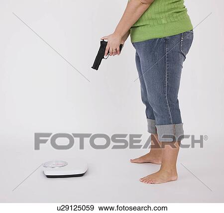 Overweight woman aiming with gun to weight scales, low section View Large Photo Image Stock Photo - Overweight woman aiming with gun to weight scales, low section. Fotosearch