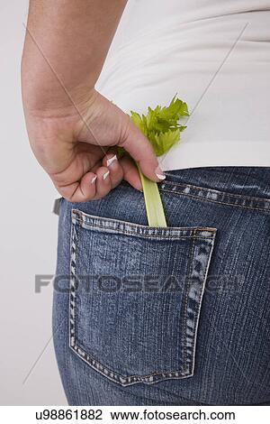 Stock Image - Overweight woman with celery in back jeans pocket, mid section, rear view. Fotosearch