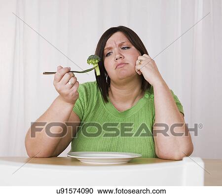 Stock Image - Overweight young woman eating broccoli. Fotosearch