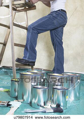 Paint cans on drop cloth covered floor, man painting wall in background, low section View Large Photo Image Picture - Paint cans on drop cloth covered floor, man painting wall in background, low section. Fotosearch