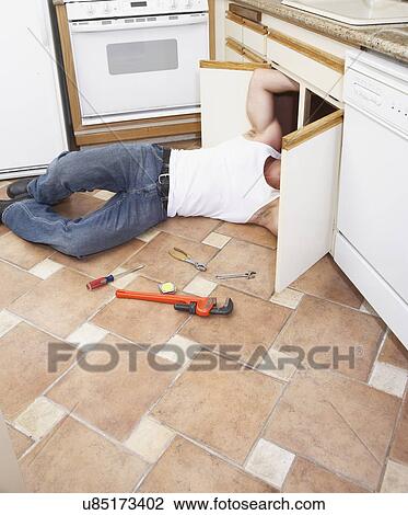 Stock Image - Plumber fixing kitchen sink. Fotosearch
