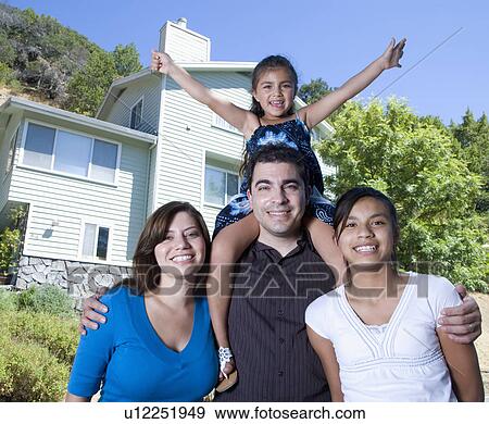 Stock Photo - Portrait of family with two girls (8-9, 14-15) in front of house. Fotosearch