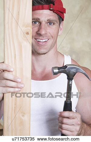 Stock Photography - Portrait of man holding piece of wood and hammer. Fotosearch