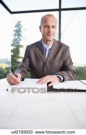 Stock Image - Portrait of mid adult businessman signing document, smiling. Fotosearch