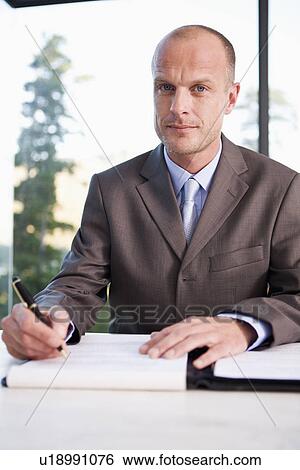 Stock Photograph - Portrait of mid adult businessman signing document. Fotosearch