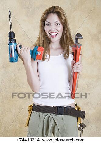 Picture - Portrait of smiling woman holding power drill and wrench . Fotosearch