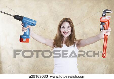 Stock Image - Portrait of smiling woman holding power drill and wrench . Fotosearch