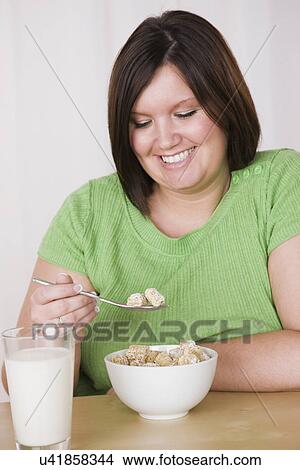 Picture - Portrait of smiling young woman eating healthy breakfast. Fotosearch