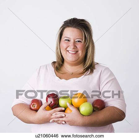 Stock Photograph - Portrait of smiling young woman holding fruits. Fotosearch