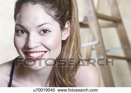 Stock Photography - Portrait of smiling young woman, ladder in background. Fotosearch