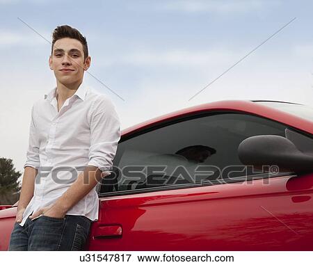 Portrait of young man standing next to red car View Large Photo Image Stock Photo - Portrait of young man standing next to red car. Fotosearch