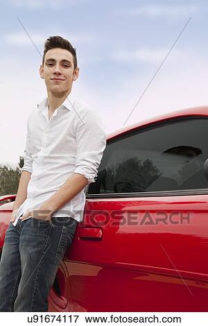 Stock Photo - Portrait of young man standing next to red car. Fotosearch