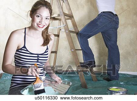 Portrait of young woman holding paint tray, man in background View Large Photo Image Stock Image - Portrait of young woman holding paint tray, man in background. Fotosearch