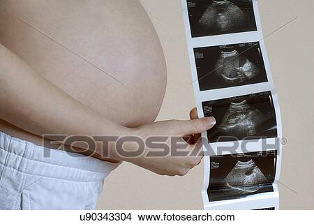 Picture - Pregnant woman holding ultrasound scan, mid section. Fotosearch