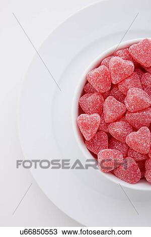 Stock Image - Red heart shape candies in bowl on white background. Fotosearch