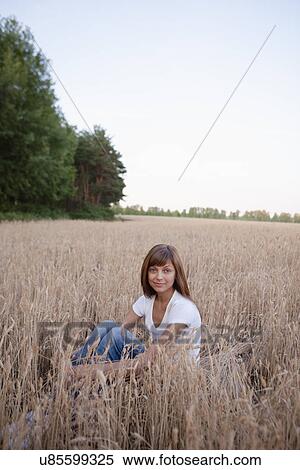 Stock Photography - Russia, Voronezh, portrait of young woman sitting in wheat field. Fotosearch