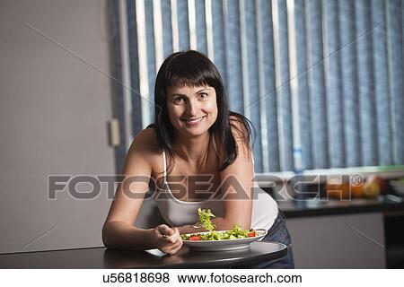 Stock Photo - Russia, Voronezh, woman eating salad in kitchen. Fotosearch