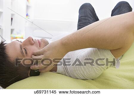 Russia, Voronezh, Young man lying on bed and talking on mobile phone View Large Photo Image Stock Photography - Russia, Voronezh, Young man lying on bed and talking on mobile phone. Fotosearch