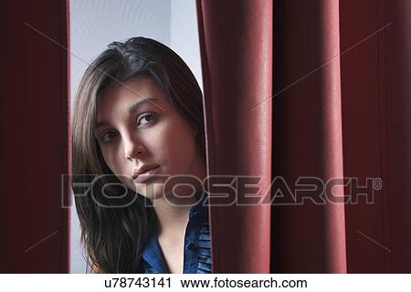 Stock Image - Russia, Voronezh, Young woman peeking through curtain. Fotosearch
