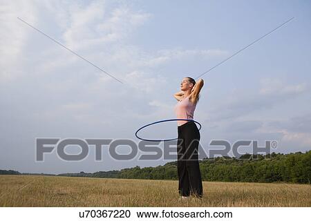 Stock Image - Russia, Voronezh, young woman exercising with hula hoop in field. Fotosearch