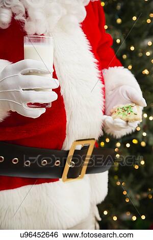 Stock Photograph - Santa Claus holding glass of milk and cookie. Fotosearch