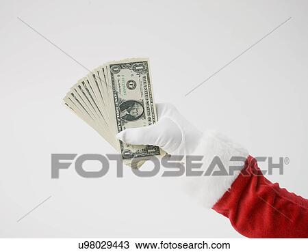 Stock Image - Santa Claus holding up dollar bills, close-up of hand. Fotosearch