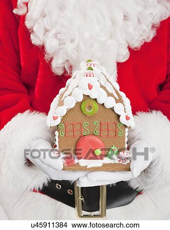 Picture - Santa clause holding gingerbread house. Fotosearch