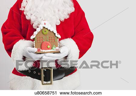 Stock Image - Santa clause holding gingerbread house. Fotosearch